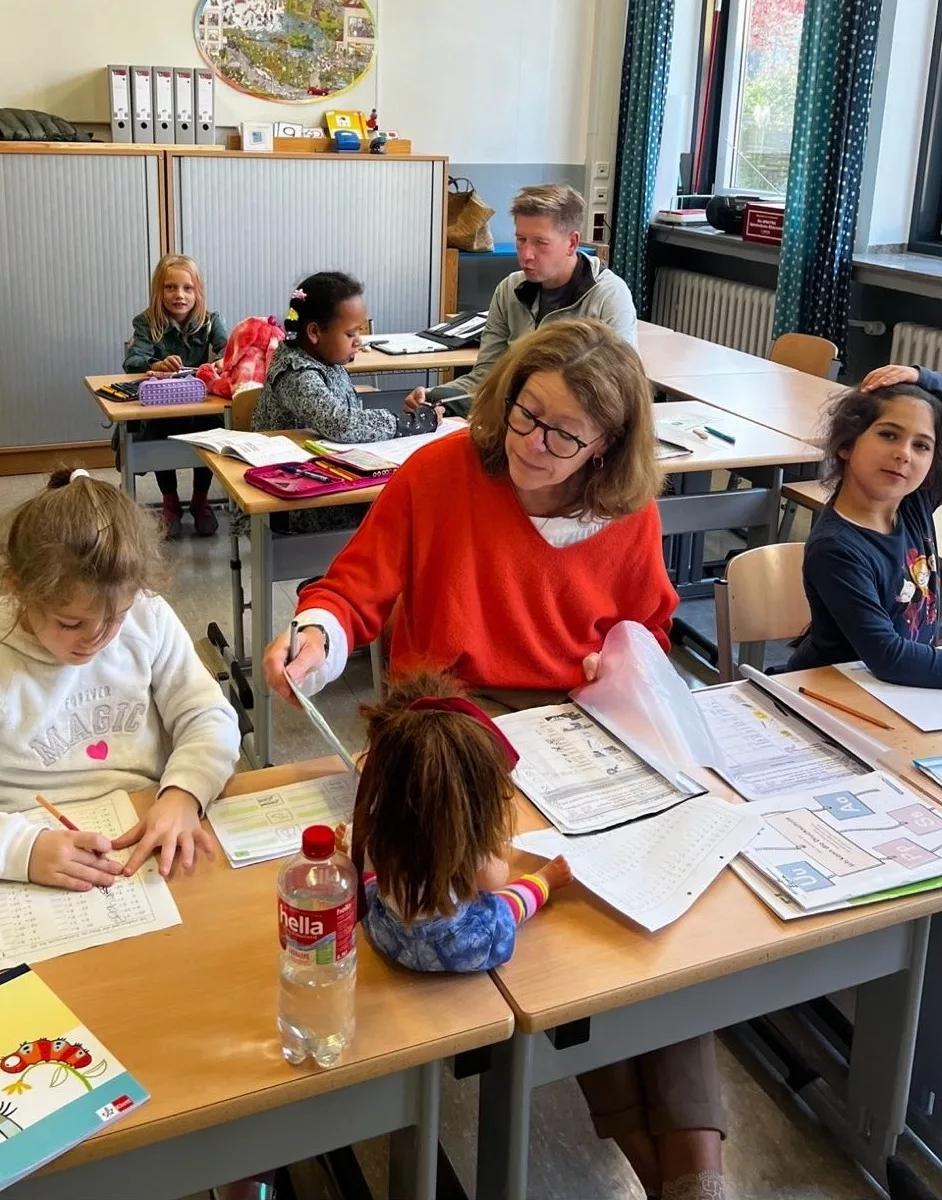 satt & schlau - Bild für den Bildlauf am Ende der Startseite - Es zeigt eine Schulklasse mit Kindern beim lernen welche von zwei Lehrkräften unterstützt werden.