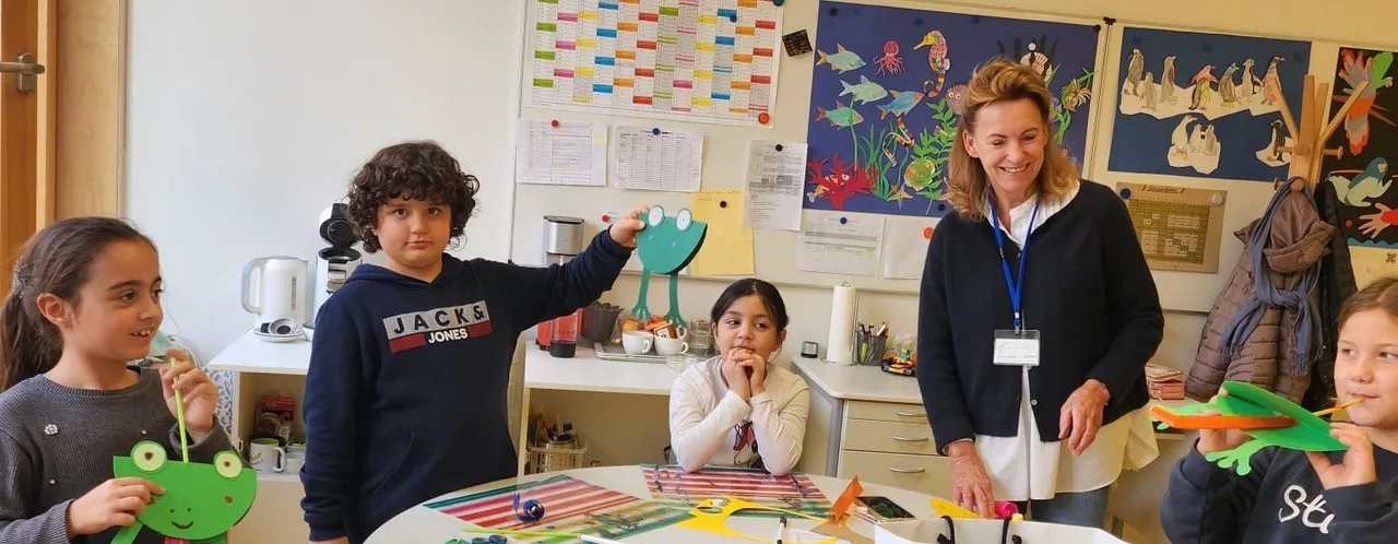 satt & schlau - Bild für die Seite "Kuratorium" - Es zeigt eine Klasse mit Kindern und einer Lehrkraft die künstlerisch tätig waren und einen Frosch aus Pappe gebastelt haben.